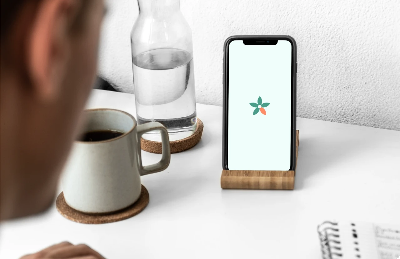 Bloom app open on a phone stand on a desk beside a water bottle and coffee mug
